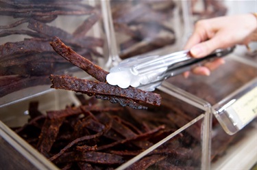 Beef jerky being held with tongs at Jerky House in Dutton Plaza