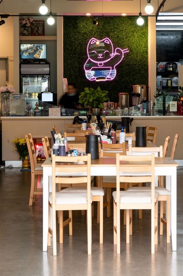 Table, seating, counter and neon wall feature of restaurant's cat logo inside Lucky Cat Vietnamese Restaurant at Dutton Plaza