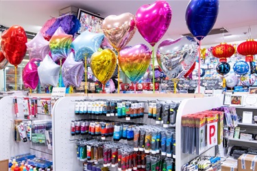 Inside Mitchum Newsagency at Dutton Plaza showing range of products including P plate car magnets, paints, Asian lanterns and chrome party balloons