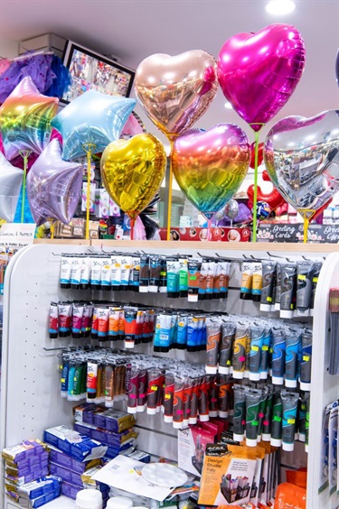 Inside Mitchum Newsagency at Dutton Plaza showing range of products including paints and chrome party balloons