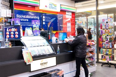 Lady buying something from the counter at Mitchum Newsagency in Dutton Plaza, with various Lotto adverts on display around the counter