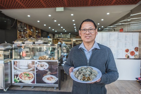 Man holding plate full of dumplings out the front of Li's Wok restaurant in Dutton Plaza